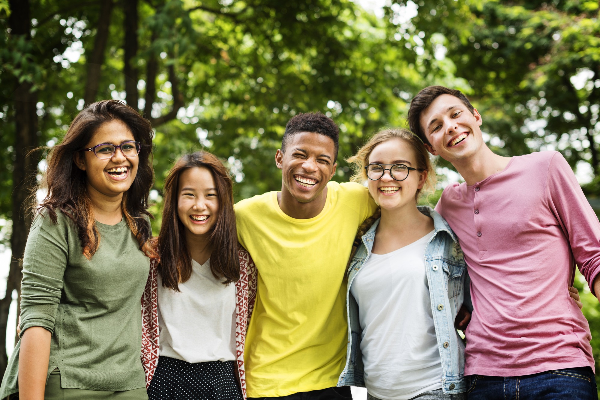 A diverse group of young individuals smiling joyfully together in a sunny park setting